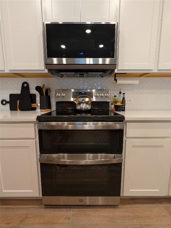 interior space featuring white cabinetry, stainless steel appliances, decorative backsplash, and light countertops