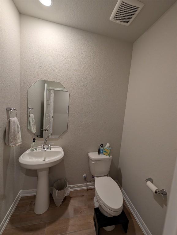 half bathroom featuring baseboards, visible vents, wood finished floors, and toilet