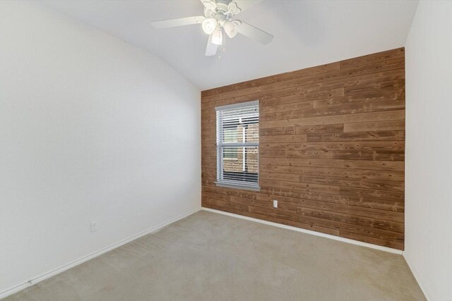 unfurnished room with carpet floors, baseboards, wooden walls, and vaulted ceiling