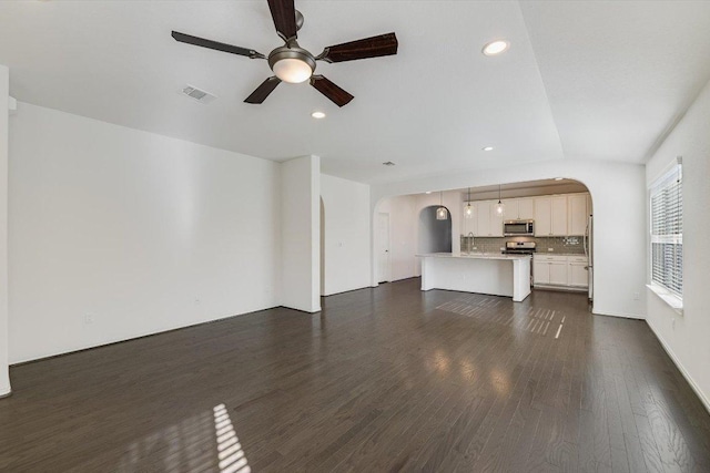 unfurnished living room featuring a ceiling fan, visible vents, arched walkways, recessed lighting, and dark wood-type flooring