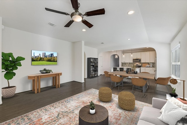 living area featuring dark wood-style flooring, arched walkways, ceiling fan, and visible vents
