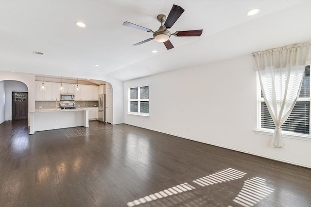 unfurnished living room with ceiling fan, visible vents, arched walkways, recessed lighting, and dark wood-type flooring