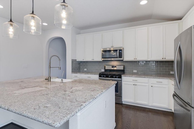 kitchen featuring a sink, tasteful backsplash, arched walkways, dark wood finished floors, and appliances with stainless steel finishes