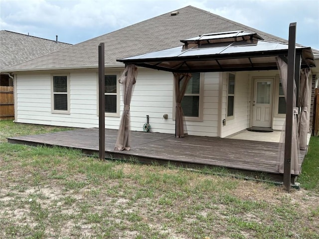 rear view of property featuring a deck, a gazebo, and a shingled roof