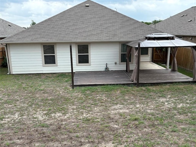 back of property with a yard, a gazebo, a wooden deck, and roof with shingles