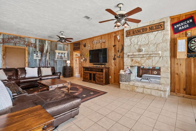 tiled living area featuring a fireplace, ceiling fan, wood walls, ornamental molding, and a textured ceiling