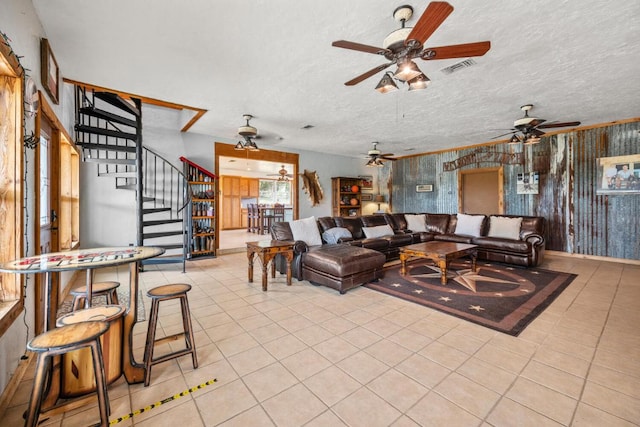 living area featuring ceiling fan, tile patterned floors, stairs, visible vents, and a textured ceiling