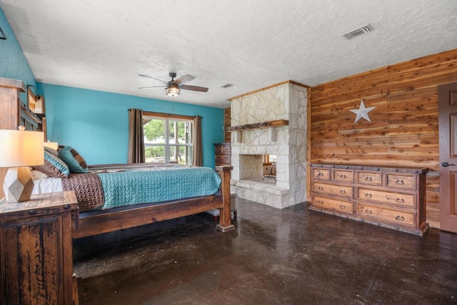 bedroom featuring concrete flooring, visible vents, a stone fireplace, wood walls, and a textured ceiling