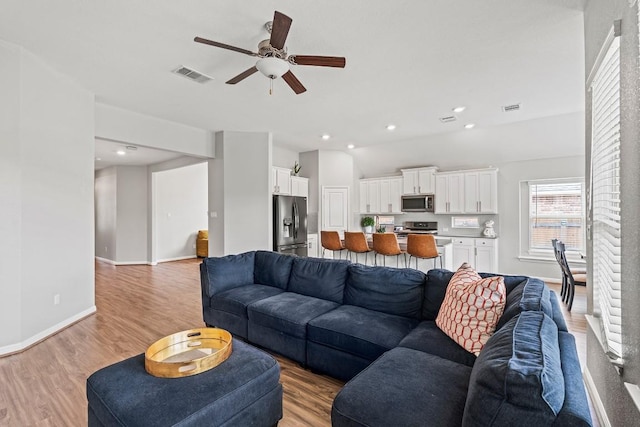 living room with baseboards, visible vents, a ceiling fan, and light wood finished floors