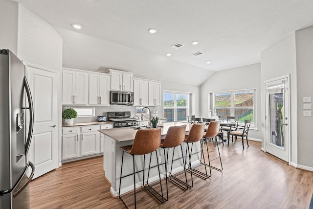 kitchen with lofted ceiling, a kitchen breakfast bar, visible vents, stainless steel appliances, and an island with sink