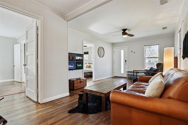 living room with crown molding, ceiling fan, visible vents, baseboards, and wood finished floors