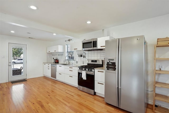 kitchen featuring appliances with stainless steel finishes, white cabinets, backsplash, a sink, and light wood-type flooring