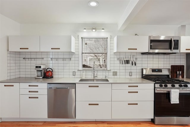 kitchen with white cabinets, stainless steel appliances, decorative backsplash, and a sink