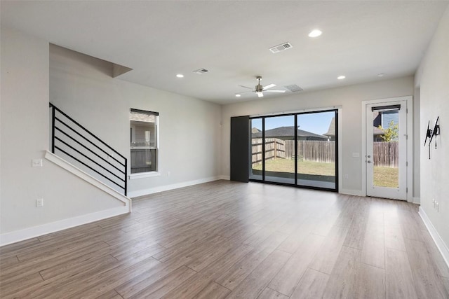 unfurnished living room featuring stairway, a ceiling fan, visible vents, baseboards, and wood finished floors