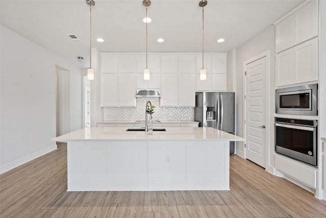 kitchen with appliances with stainless steel finishes, light wood-style floors, visible vents, under cabinet range hood, and backsplash
