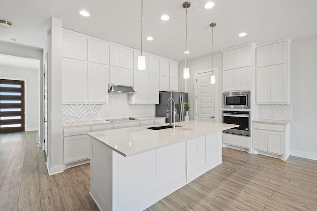 kitchen featuring tasteful backsplash, light wood-style floors, appliances with stainless steel finishes, and a center island with sink