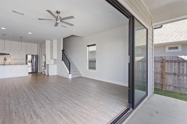unfurnished living room featuring wood finished floors, visible vents, a ceiling fan, and baseboards