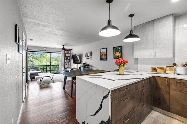 2605 Enfield Rd Unit 209, Austin, TX 78703 - kitchen featuring ceiling fan, a peninsula, a textured wall, light wood finished floors, and light stone counters