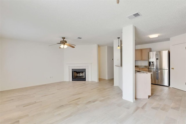 unfurnished living room with light wood finished floors, a textured ceiling, a tiled fireplace, a ceiling fan, and visible vents
