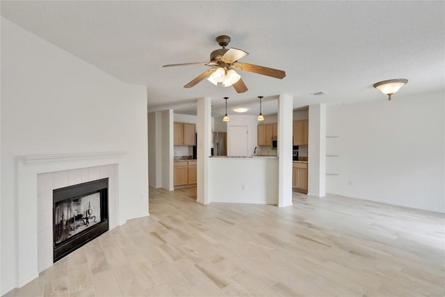 2009 Barnett Dr, Cedar Park, TX 78613 - unfurnished living room with a ceiling fan, a tile fireplace, light wood finished floors, and a textured ceiling