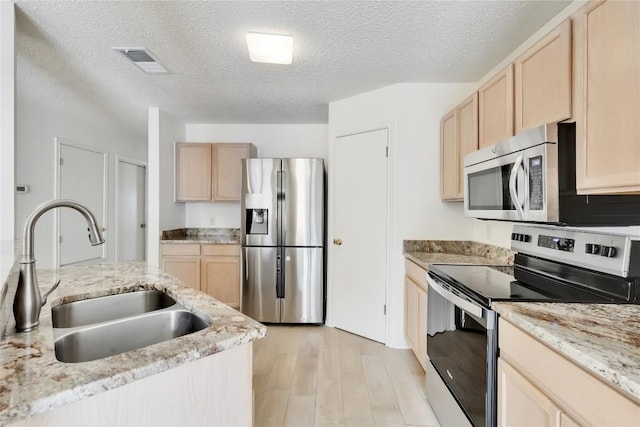 2009 Barnett Dr, Cedar Park, TX 78613 - kitchen with stainless steel appliances, a sink, light brown cabinetry, light wood-style floors, and a textured ceiling