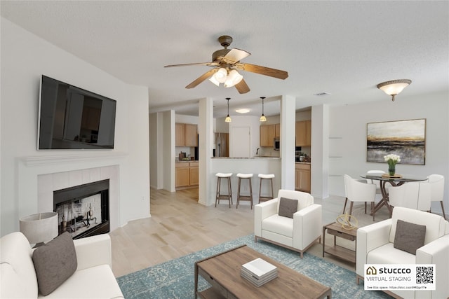 2009 Barnett Dr, Cedar Park, TX 78613 - living room featuring ceiling fan, light wood finished floors, a textured ceiling, and a tile fireplace