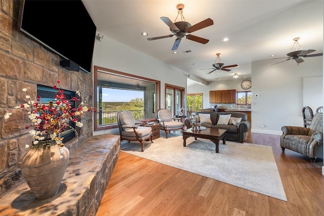 living room with wood finished floors, a ceiling fan, a stone fireplace, and recessed lighting