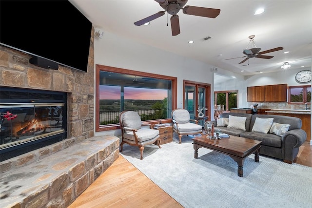 living area with recessed lighting, a ceiling fan, a stone fireplace, and wood finished floors