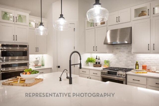 321 Dycus Bnd, Liberty Hill, TX 78642 - kitchen with wall chimney exhaust hood, stainless steel appliances, tasteful backsplash, white cabinetry, and pendant lighting