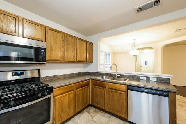 17928 Honey Locust Ln, Elgin, TX 78621 - kitchen featuring appliances with stainless steel finishes, dark countertops, a peninsula, brown cabinetry, and arched walkways