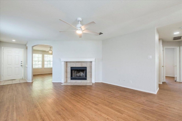 109 David Dr, Hutto, TX 78634 - unfurnished living room with ceiling fan, light wood-type flooring, baseboards, arched walkways, and a tile fireplace