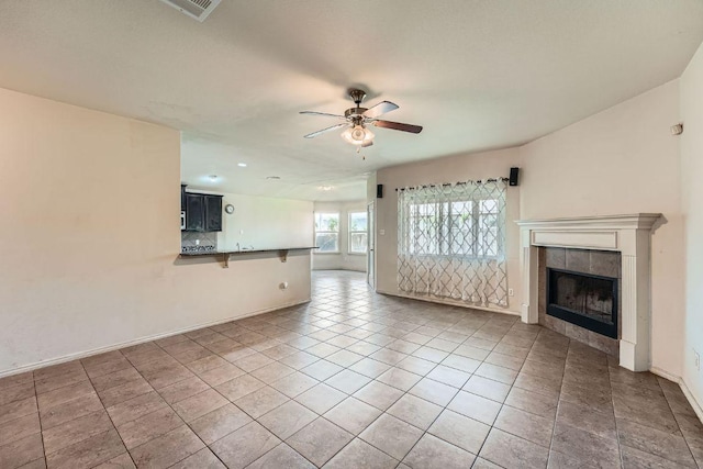 unfurnished living room with a tiled fireplace, baseboards, visible vents, a ceiling fan, and light tile patterned flooring