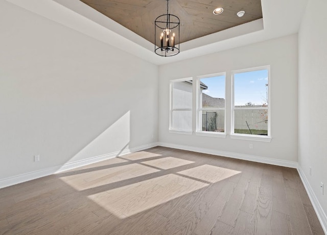 109 Flora Springs Cv, Liberty Hill, TX 78642 - empty room featuring a tray ceiling, baseboards, a chandelier, and wood finished floors