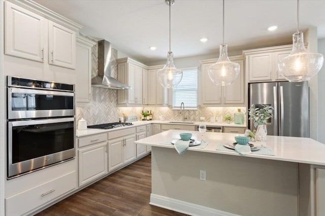 kitchen with wall chimney range hood, dark wood-type flooring, light countertops, a sink, and stainless steel appliances