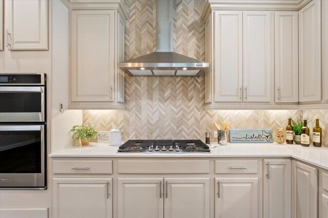 kitchen with light countertops, wall chimney exhaust hood, appliances with stainless steel finishes, and decorative backsplash