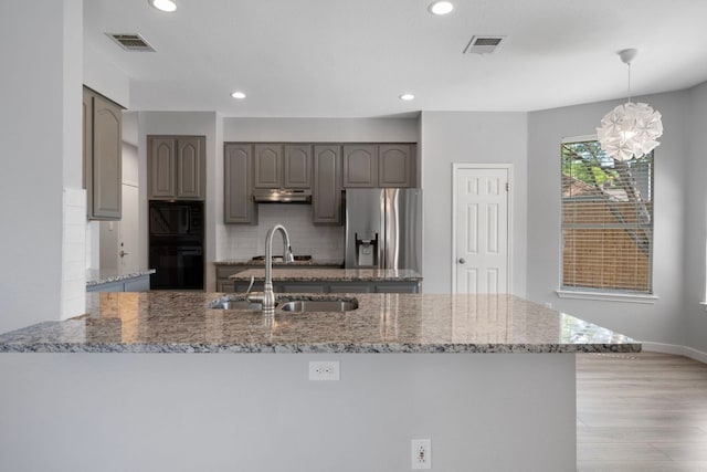 kitchen with tasteful backsplash, a sink, visible vents, under cabinet range hood, and black appliances