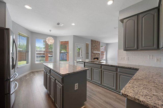 kitchen featuring a sink, dishwashing machine, stainless steel refrigerator with ice dispenser, light stone counters, and a peninsula