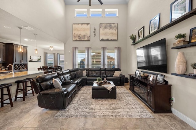 living room with baseboards, visible vents, ceiling fan, and a towering ceiling