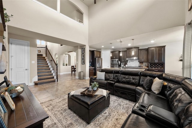 living area with baseboards, stairway, arched walkways, and a high ceiling