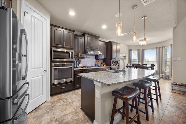 kitchen with light stone countertops, a sink, stainless steel appliances, decorative backsplash, and dark brown cabinetry