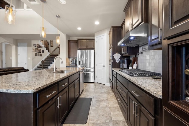 kitchen with a sink, stainless steel appliances, under cabinet range hood, backsplash, and dark brown cabinets
