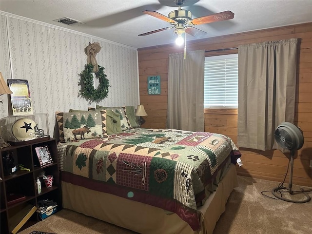 carpeted bedroom with visible vents, ornamental molding, ceiling fan, and wood walls