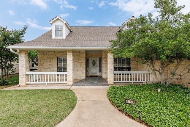 view of front of house featuring roof with shingles, covered porch, a front yard, and stone siding