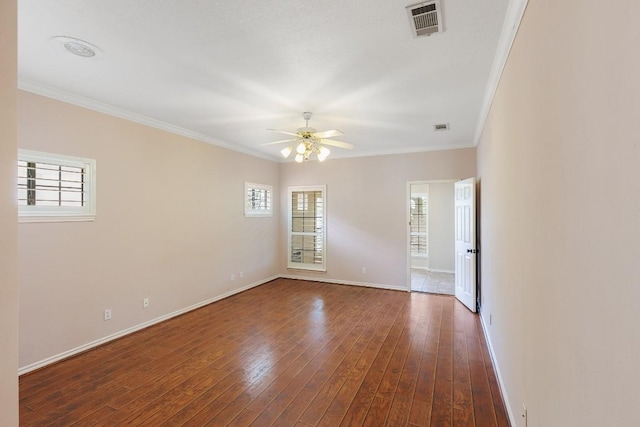 spare room with crown molding, visible vents, baseboards, dark wood-style floors, and a ceiling fan