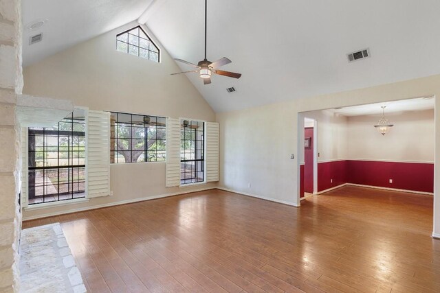 unfurnished living room featuring a ceiling fan, visible vents, high vaulted ceiling, baseboards, and hardwood / wood-style floors