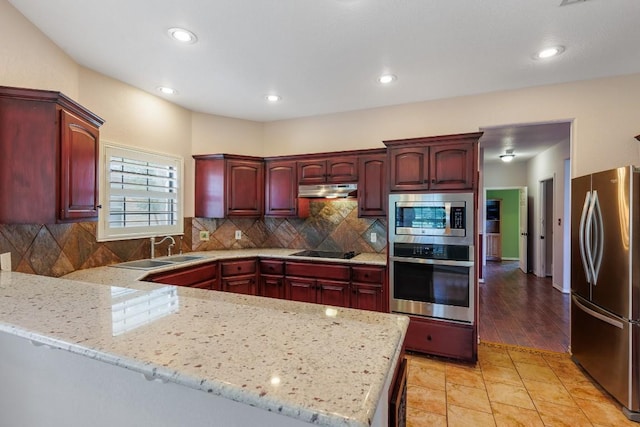 kitchen with a peninsula, dark brown cabinets, under cabinet range hood, a sink, and appliances with stainless steel finishes