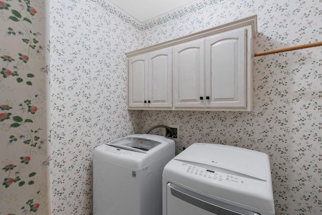 laundry area featuring cabinet space, wallpapered walls, and washer and clothes dryer