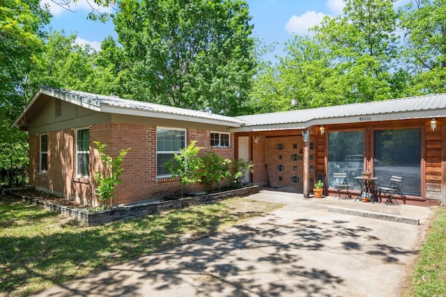ranch-style home featuring brick siding, metal roof, and a patio area