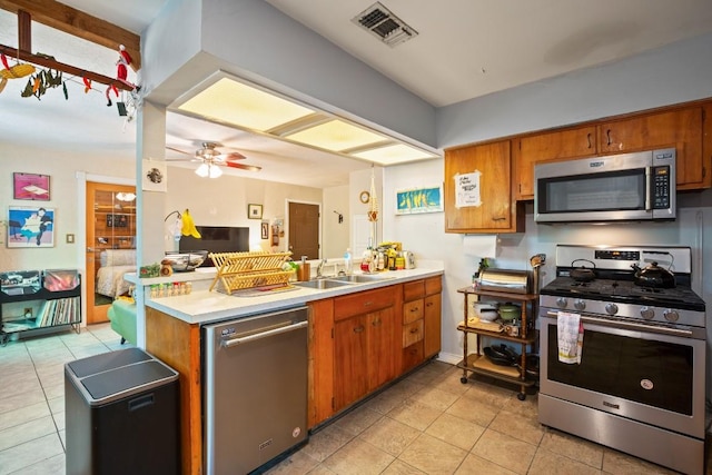kitchen with visible vents, stainless steel appliances, light tile patterned flooring, a peninsula, and brown cabinetry