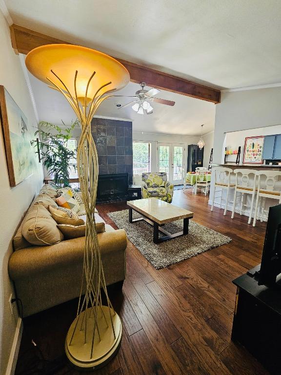 living area featuring wood finished floors, ceiling fan, a tile fireplace, and beamed ceiling
